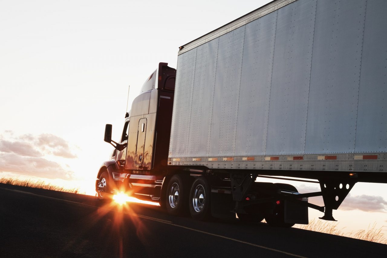 silhouette of a commercial truck driving on a highway at sunset